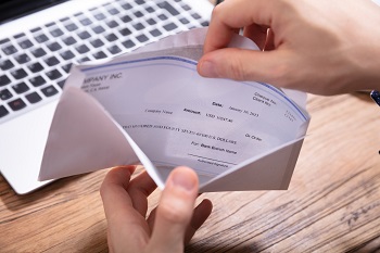 Person looking in envelope containing paycheck with keyboard in background